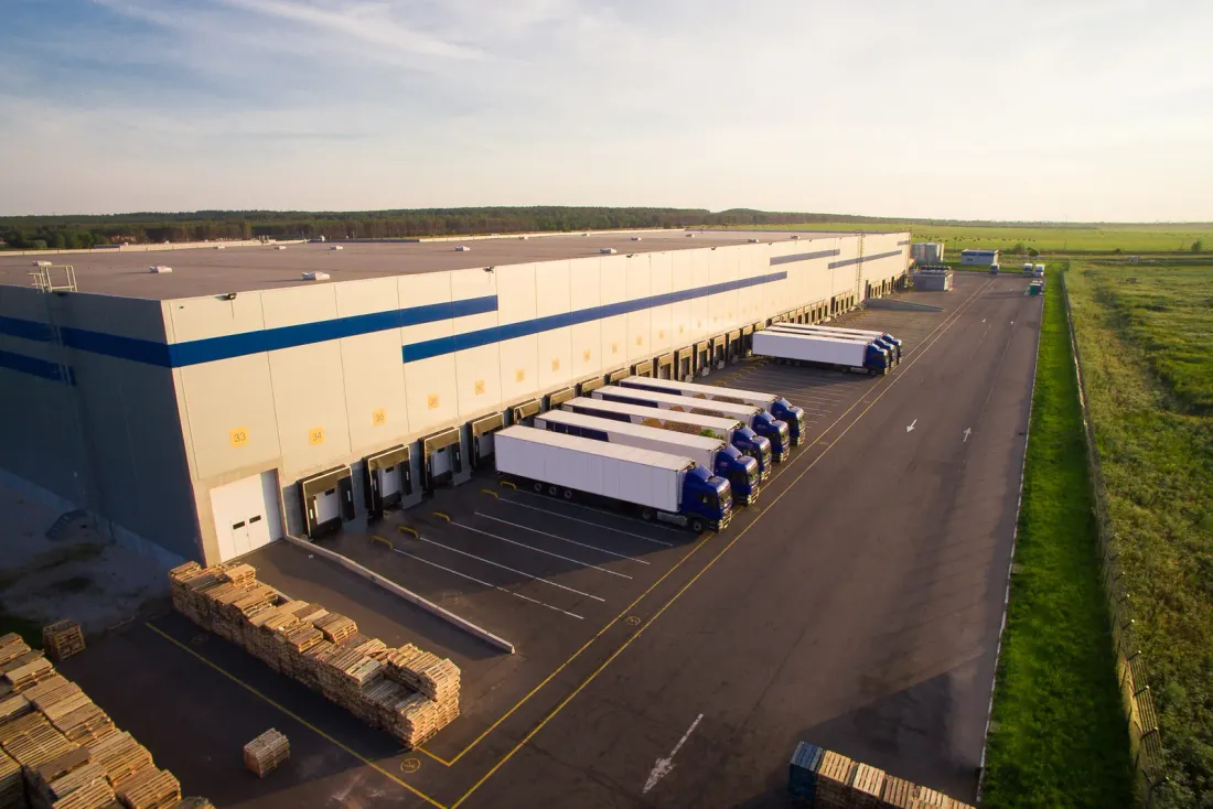 An aerial view of a long distribution warehouse with semi-trailers at its loading docks and stacked pallets in the yard, a setting for commercial cleaning services in El Cajon, CA